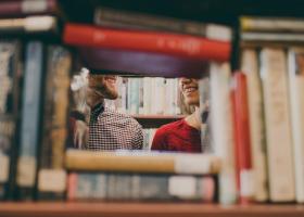 la vista parcial de un hombre y una mujer sonriendo a través de un hueco entre pilas de libros