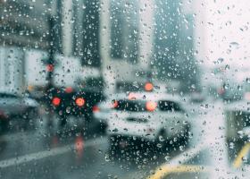 Vista de una avenida con autos en pavimento mojado a través del parabrisas de auto con gotas de lluvia 