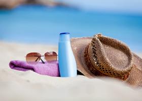 Sombrero, lentes, toalla y bloqueador solar sobre arena en una playa