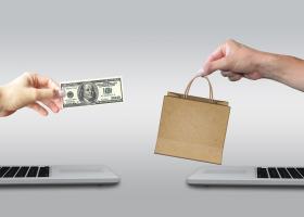 imagen de dos pantallas de computadoras, una frente a la otra, de donde emergen manos humanas intercambiando productos por dinero, ilustrando negocios por internet.