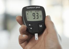 Persona sosteniendo en la mano un aparato de medición de glucosa en sangre Contour Plus, imagen de Ascensia