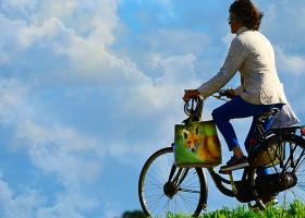 Mujer con pantalones montada en bicicleta en una colina de pasto verde con el cielo azul al fondo