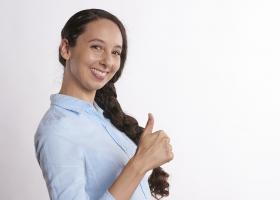 mujer joven con camisa de trabajo sonriendo y levantando el pulgar