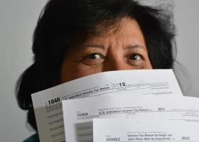 Mujer de mirada feliz con formatos de pago de impuestos tapando parte de su rostro