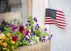 imagen de una ventana con jardinera con flores y una pequeña bandera norteamericana en la jardinera