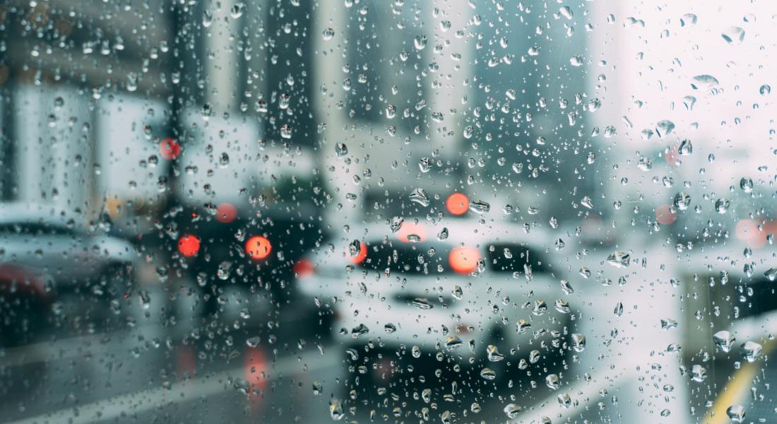 Vista de una avenida con autos en pavimento mojado a través del parabrisas de auto con gotas de lluvia 