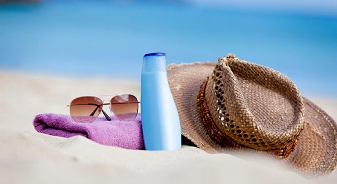 Sombrero, lentes, toalla y bloqueador solar sobre arena en una playa
