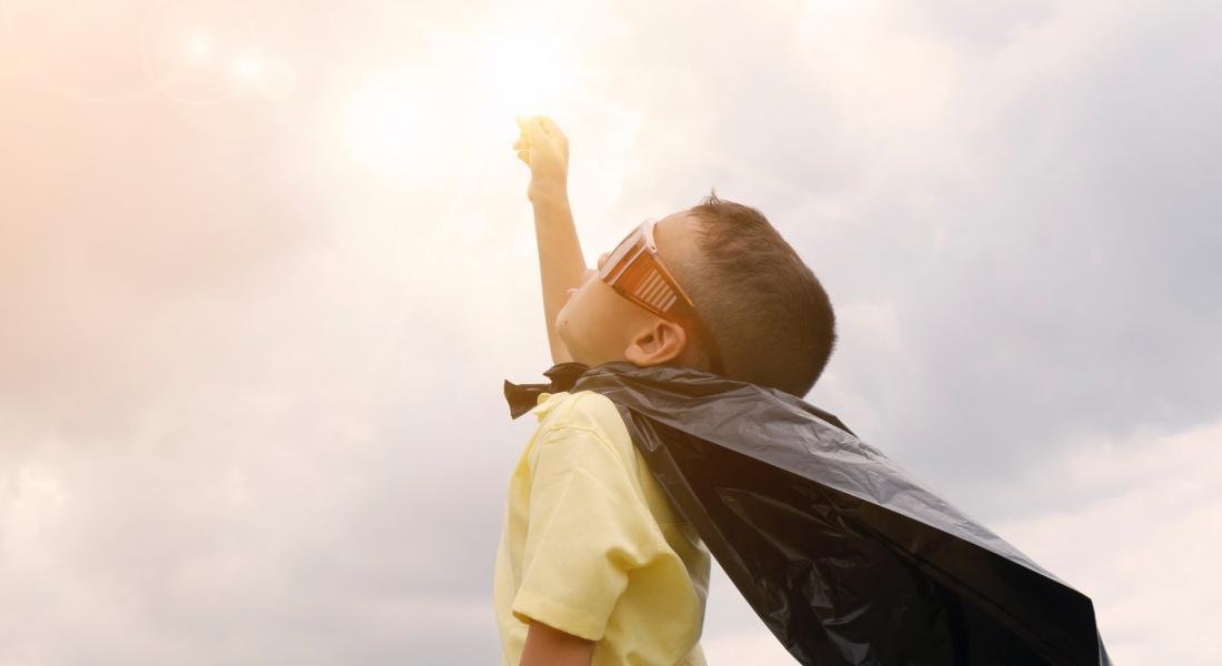 niño con capa de superhéroe levantando su puño hacia el cielo