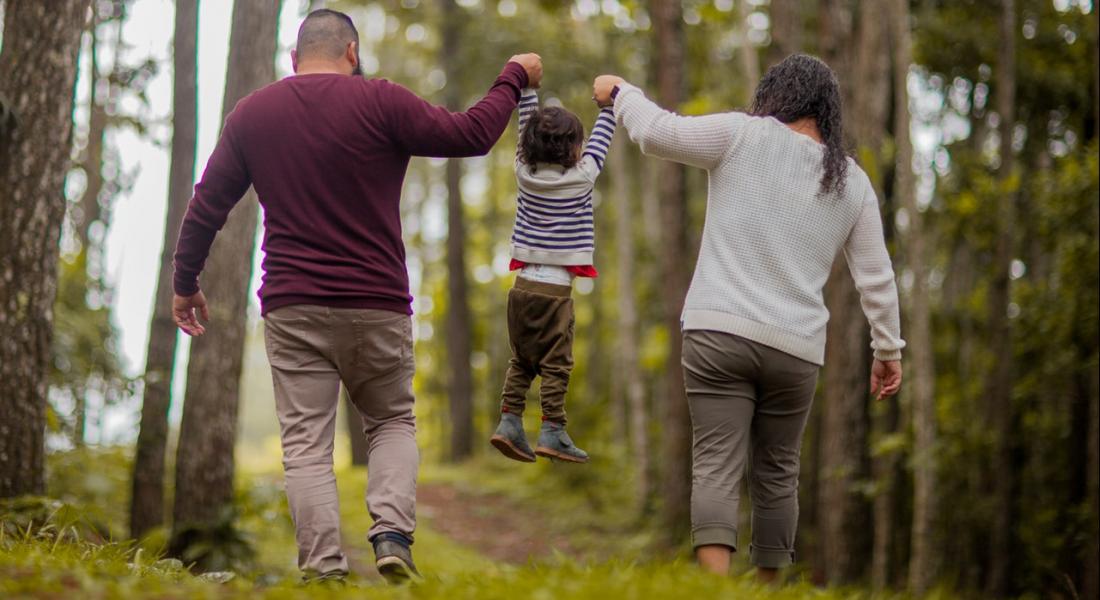 Familia de mamá, papá e hijo caminando en el bosque tomados de la mano