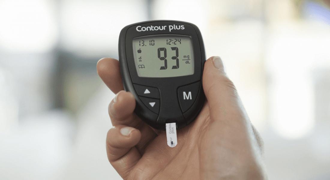 Persona sosteniendo en la mano un aparato de medición de glucosa en sangre Contour Plus, imagen de Ascensia