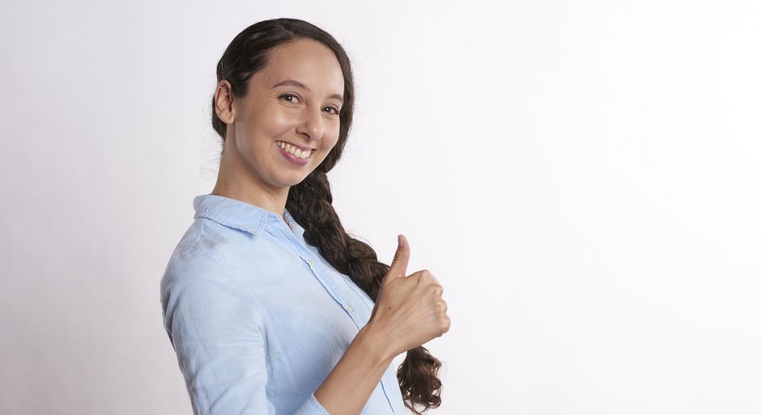 mujer joven con camisa de trabajo sonriendo y levantando el pulgar