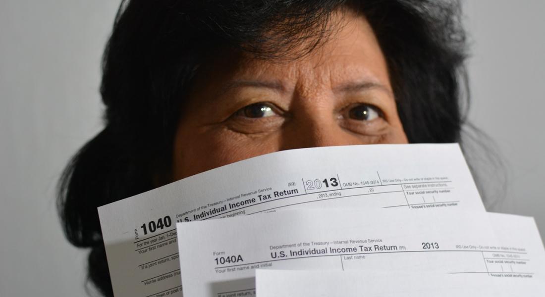 Mujer de mirada feliz con formatos de pago de impuestos tapando parte de su rostro