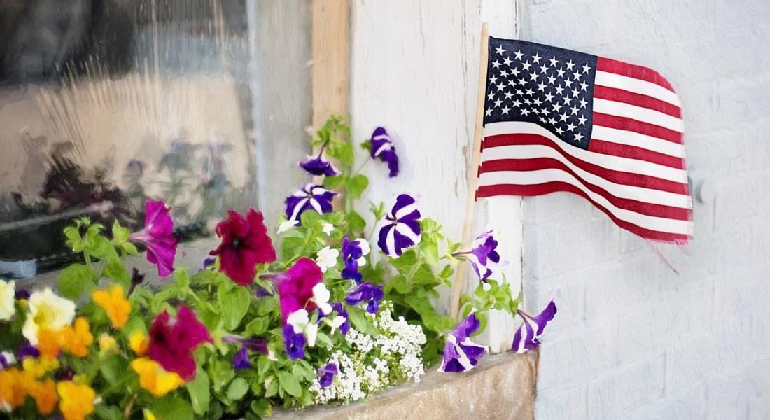 imagen de una ventana con jardinera con flores y una pequeña bandera norteamericana en la jardinera