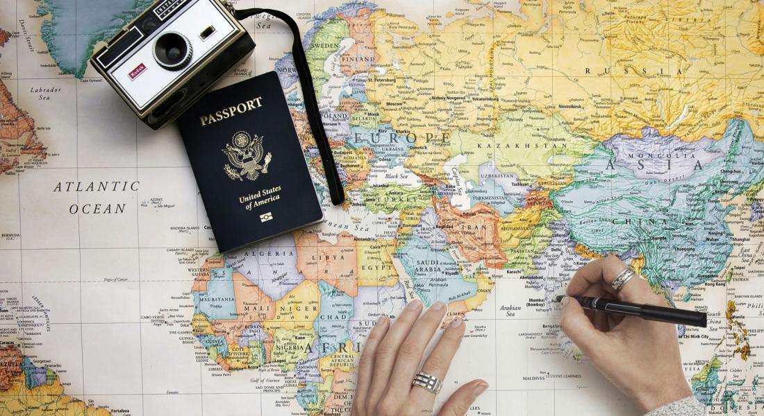 Persona marcando destinos en un mapa de papel, donde se ven también un pasaporte norteamericano y una cámara fotográfica