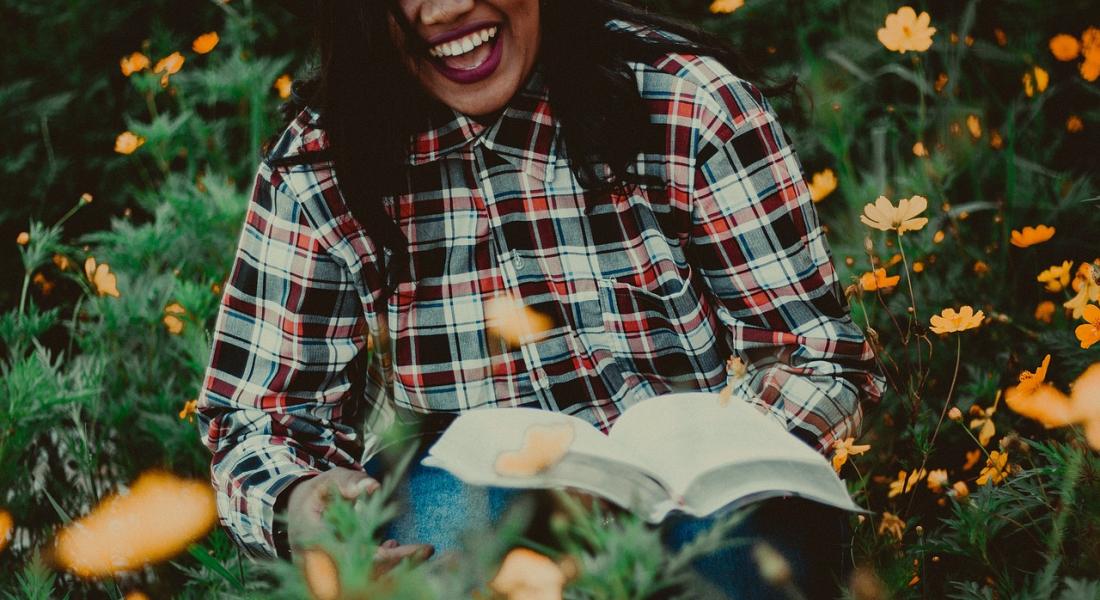 Mujer riendo mientras sostiene un libro en sus manos